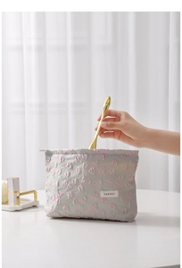Detail of floral quilted makeup bag in grey showing texture and brand label