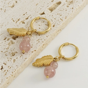 Detailed shot of golden feather hoop earrings with pink crystal beads on a stone pedestal