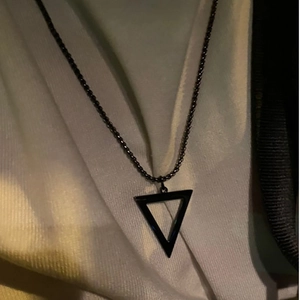 Close-up of a black hollow triangle pendant on a chain over white textured fabric