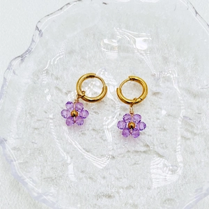 Handmade gold flower earrings with purple faceted beads on a matte glass tray