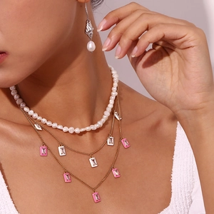 Detail of gold layered necklaces with pink enamel pendant and white pearl choker on model