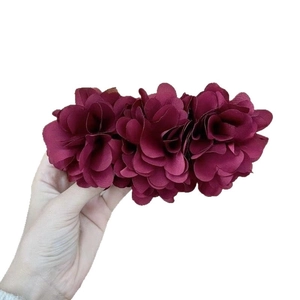 Handheld view of a large burgundy fabric triple flower hair clip on a white background