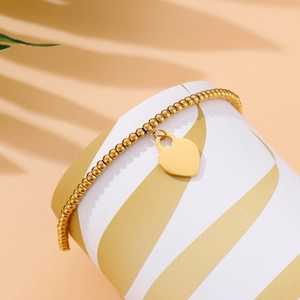 Detail of 18k gold beaded bracelet with a smooth heart pendant on a decorative stand
