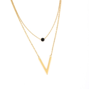 Detail einer goldene Doppelkette mit schwarzem Edelstein und V-förmigem Metallanhänger