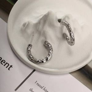 Detail of silver C-shape earrings with irregular lava texture on white stone display