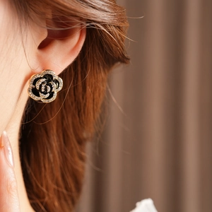 Close-up of black camellia flower earrings with gold frame and sparkling rhinestones