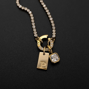 Close-up of gold-plated necklace with crystal-encrusted letter P and square gemstone.