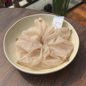 Detail of cream mesh scrunchie with natural small shells on a decorative ceramic plate