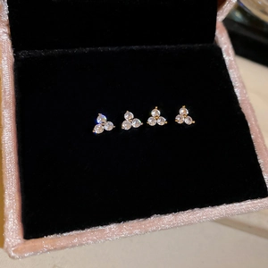 Close-up of four gold flower stud earrings with white zircons on black velvet