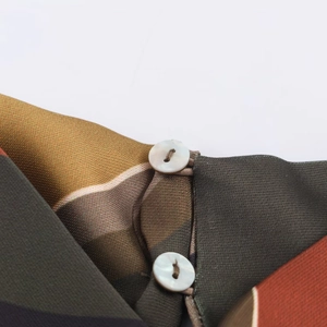 Détail macro du tissu à rayures multicolores avec boutons nacrés sur un haut asymétrique