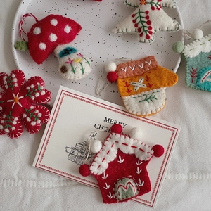 Close-up of wool felt Christmas ornaments including red house, mushroom, and glove