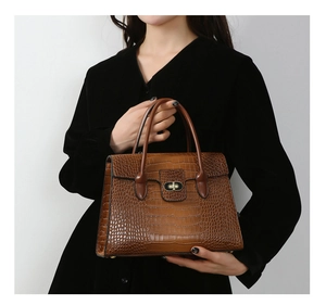 Detail showing brown crocodile pattern leather texture and metal buckle on a shoulder bag