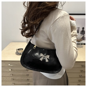 Close-up of glossy black shoulder bag with silver bow detail and gold zipper finish