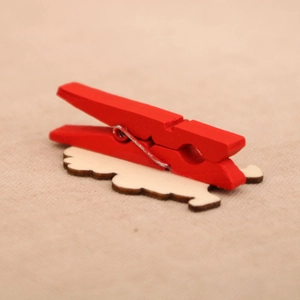 Close-up of red wooden Christmas clip with white cloud base on a beige fabric background