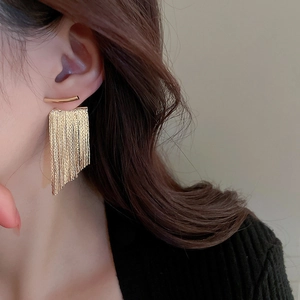 Close-up of golden long chain tassel earrings worn by a model for elegant metal style