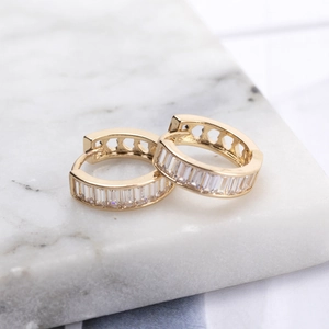 Elegant gold round earrings with baguette CZ stones and heart cut-outs on marble base