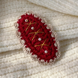 Macro shot of handmade red knitted hair clip with white pearls and gold accents