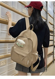 Detail view of beige canvas backpack featuring a plush cloud charm and adjustable straps