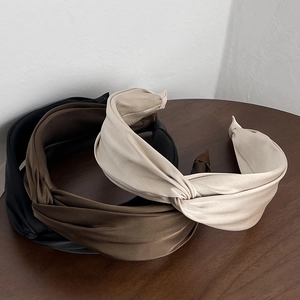 Close-up of three twisted satin headbands in black, brown, and beige on a wooden table