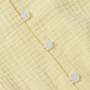 Macro shot of yellow cotton gauze fabric texture with white round button detailing