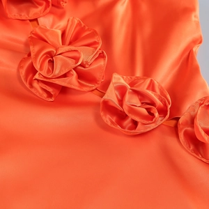 Detailed close-up of orange satin fabric with an intricate 3D floral design