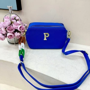 Blue leather crossbody bag with gold letter P and colorful charms on stone pedestal
