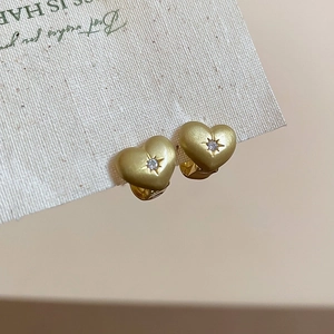 Detail of matte gold heart earrings with zircon center and starburst engraving