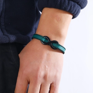 Detail of green leather bracelet with black infinity charm on a male wrist