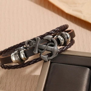Close-up of a multi-layer brown braided leather bracelet with silver anchor charm on a box