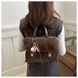 Dettaglio di uno zaino vintage in pelle marrone con fibbie argentate e un ciondolo da baseball