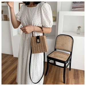 Detail of box-shaped straw handbag featuring retro bamboo handles and black leather flap