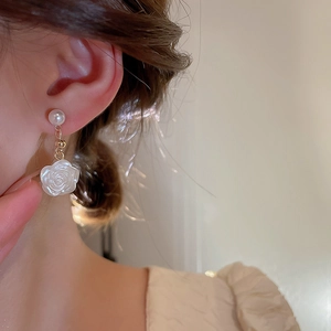 Close-up of pearl and white acrylic camellia flower drop earrings on a model