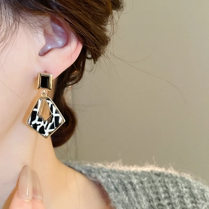 Détail d'un mannequin portant des boucles d'oreilles géométriques à rectangle noir et losange