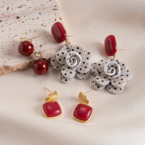 Detail of red square studs, floral polka dot earrings, and beaded drop on silk fabric