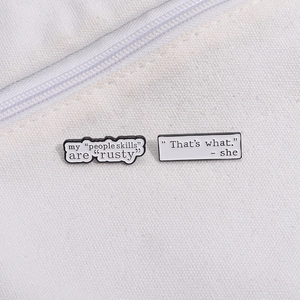 Detail showing two white enamel pins with humorous text on a white canvas bag texture