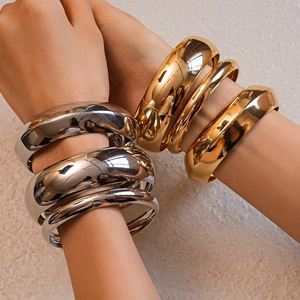 Close-up of stacked gold and silver chunky metal bangles with a polished mirror finish