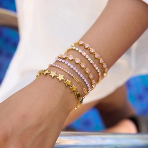 Detailed close-up of stacked gold heart and star bracelets on wrist with pink zircons