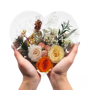 Handheld heart-shaped clear resin mold with orange and yellow roses and dried flowers