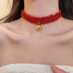 Détail d'un ras-de-cou en tricot rouge avec pendentif cloche dorée sur le cou