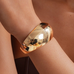 Detailansicht eines minimalistischen, polierten goldenen Armreifs am Handgelenk einer Frau
