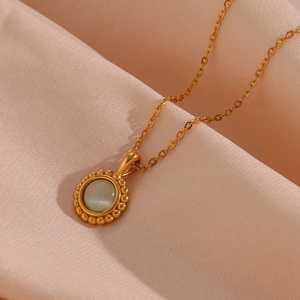 Close-up of golden necklace with vintage sunburst pendant and opal stone on pink fabric