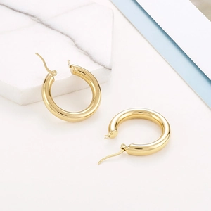 Detailed view of polished 18K gold-plated titanium steel hoop earrings on marble