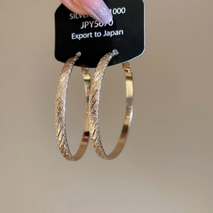Detail of gold circular hoop earrings with textured matte finish and diagonal stripe pattern