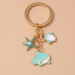 Detail of gold keychain with blue starfish, penguin, and shark enamel charms on pink background