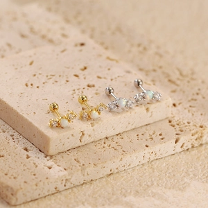 Close-up of minimalist opal ear studs with small zircon accents on a stone surface