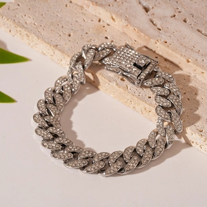 Detail of silver Cuban link bracelet with iced-out rhinestones on stone background