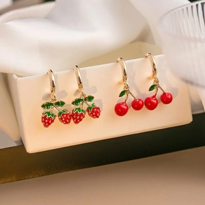 Vista macro di orecchini a forma di fragola e ciliegia sul bordo di un contenitore bianco
