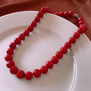 Minimalist deep red round glass bead choker necklace with metallic clasp on white plate