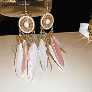 Detail of bohemian drop earrings with pink and white feathers on a glass rim