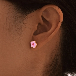 Macro shot of small pink floral stud earring with gold metal trim worn on the ear
